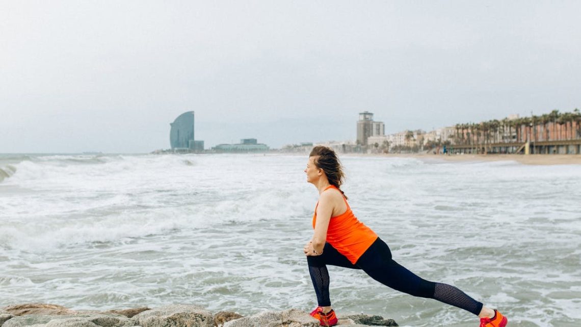 A woman stretches by the ocean in Barcelona, showcasing health and fitness by the sea.